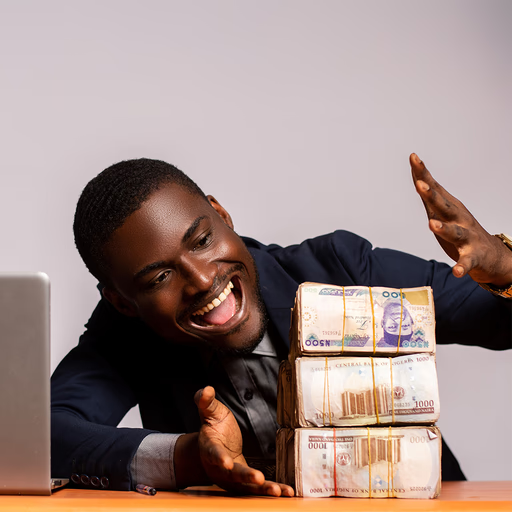 Smiling entrepreneur at a desk with naira notes and a laptop